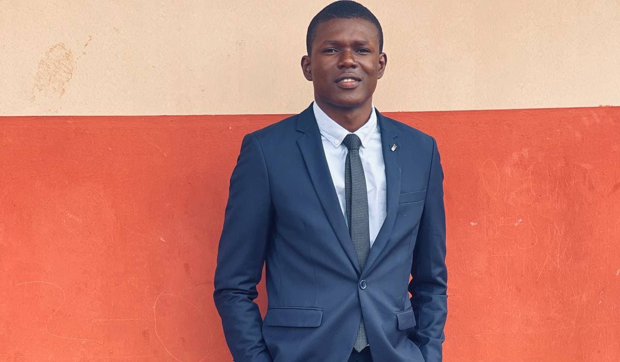 Praise Olufemi in a navy suit against a sand and red wall